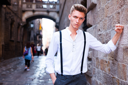 ordinary young European guy in shirt and trousers with suspenders walking around cityの写真素材