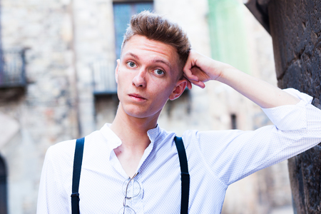 ordinary young European guy in shirt and trousers with suspenders walking around cityの写真素材