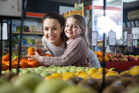 happy blonde girl with mother buying mandarins in shopの写真素材