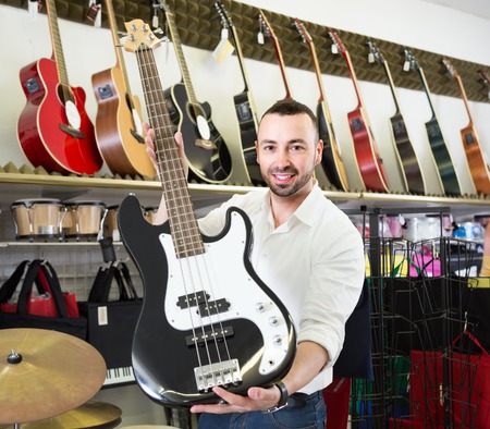 smiling guy choosing new electric guitar in musical storeの写真素材