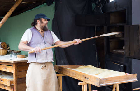 male baker puts bread on the shovel into the ovenの写真素材