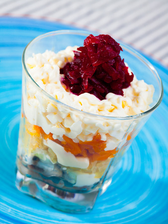 verrin glass with delicious Russian salad herring under fur coat from vegetables on blue plateの写真素材