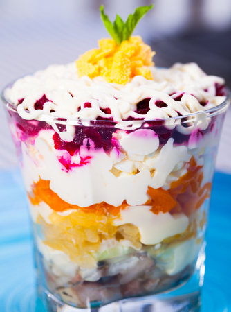 verrin glass with delicious Russian salad herring under fur coat from vegetables on blue plateの写真素材