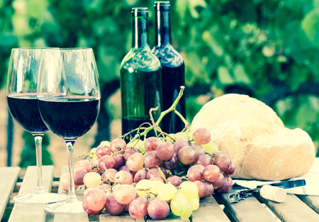 glass of red wine ripe grapes and bread on table in vineyardの写真素材