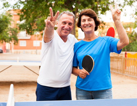 mature couple showing victory near table tennis at outdoorの写真素材