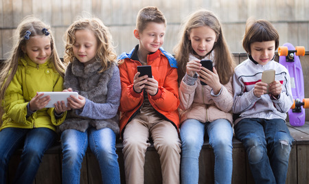 ordinary children playing with the phone on bench outdoorsの写真素材