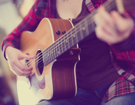Close-up girl playing guitar in music store. Focus on strings of guitar