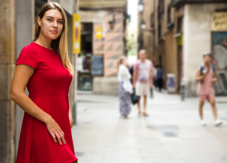 beautiful young girl in red dress walks through the old European streetsの写真素材
