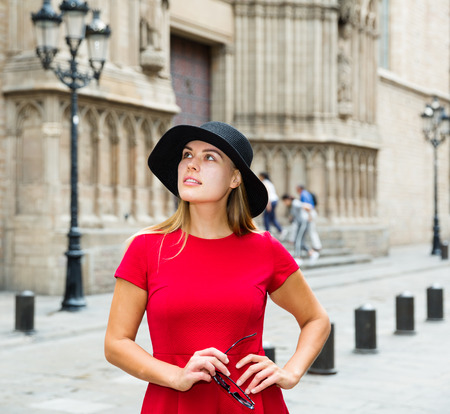 beautiful young girl in red dress walks through the old European streetsの写真素材