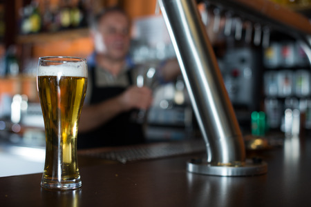 glass of beer on bar counter against background of friendly elderly bartenderの写真素材