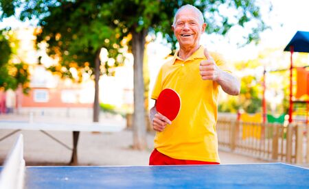 Happy mature man playing table tennis and showing thumb upの写真素材