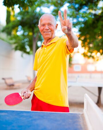 portrait of senior with rackets for table tennis showing victoryの写真素材