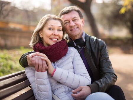 elderly couple on a bench pointing forward in a park in autumn dayの写真素材