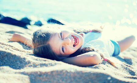 blond child girl lying on sandy beach of sea coastの写真素材