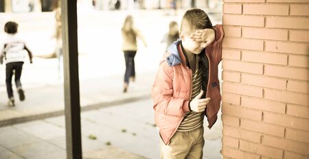 playing hide and seek. ordinary boy closed eyes his hands standing at brick wallの写真素材