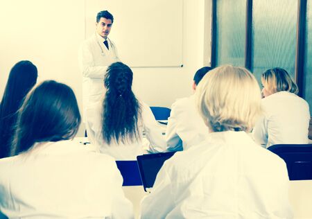 Students in white coats listen to lecture in audienceの写真素材