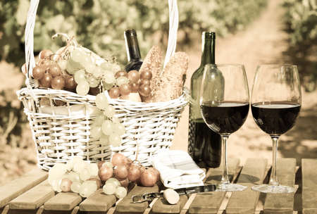 still life with glass of red wine grapes and picnic basket on table in fieldの写真素材