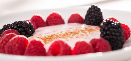 fresh raspberries and blackberries laid out on a white plate in circle with yogurt and cinnamon