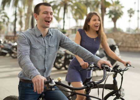 young couple guy with a girl ride bicycles with thick wheels in the summer along the promenadeの写真素材