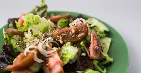 appetizing vegetable salad of greens, tomatoes and cucumbers on a green plateの写真素材