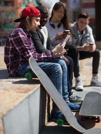 group of multinational teenagers play in smartphones in schoolyard