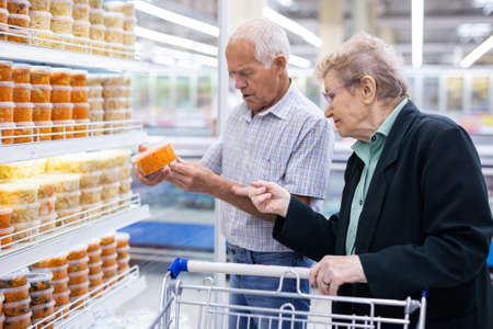 mature caucasian couple chooses pickled vegetables in the supermarket departmentの写真素材