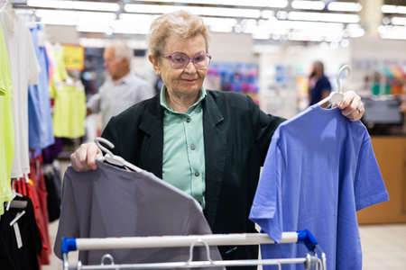 older european woman with glasses chooses blouse in clothing department of supermarketの写真素材