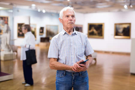 elderly European man examines paintings in an exhibition in hall of an art museumの写真素材