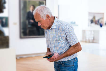 elderly European man examines paintings in an exhibition in hall of an art museumの写真素材