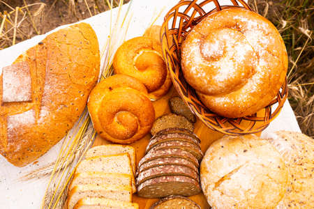 various types of fresh bread on linen tablecloth on table in cereal field outsideの写真素材