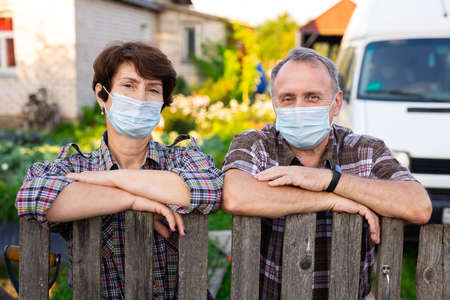 Portrait of two farmers wearing protective masks at the fence of their country houseの写真素材