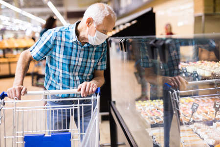 mature european man wearing mask and gloves with covid protection shoping in supermarketの写真素材