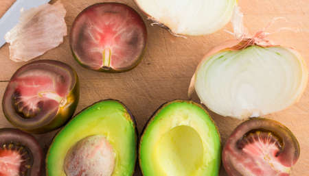 ripe vegetables black tomatoes, avocado and onions on wooden board