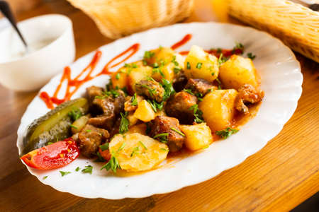 roast veal with potatoes served with pickled cucumber on a white plate