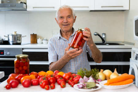 old man holding jars of pickled tomatoes and smilingの写真素材