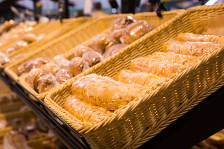 fresh breads with melted cheese wrapped in plastic wrap in wicker basket in bread department of...