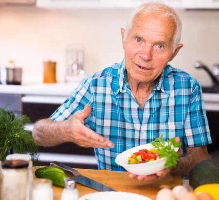 elderly european man made a fresh vegetable salad at homeの写真素材