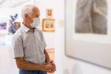 elderly European man examines paintings in an exhibition in hall of an art museumの写真素材