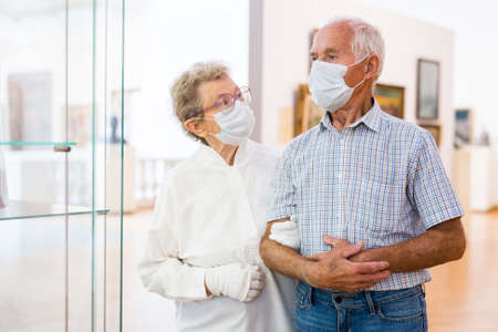 elderly European couple in mask protecting against covid examines paintings on display in hall of art museumの写真素材