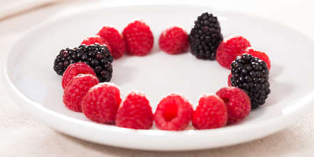 fresh raspberries and blackberries laid out on a white plate in circleの写真素材