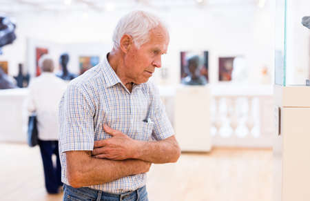 elderly European man examines paintings in an exhibition in hall of an art museumの写真素材