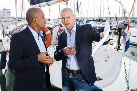 Latin American and European men with documents choosing and buying near yachts in the portの写真素材