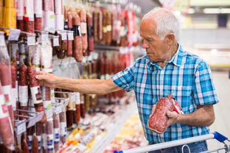 mature senor choosing uncooked smoked sausages in sausage department supermarketの写真素材