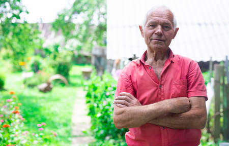 elderly senior pensioner in red polo posing near the house in the villageの写真素材