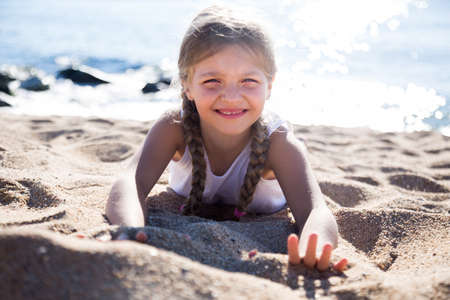 blond child girl lying on sandy beach of sea coastの写真素材
