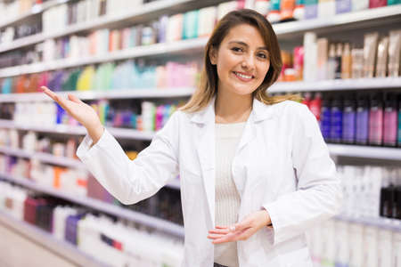 Friendly smiling female seller demonstrating various haircare cosmetics in specialized boutiqueの写真素材