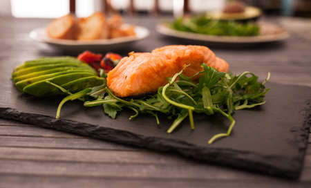 Baked sea trout fillet with fresh vegetables and herbs on black boardの写真素材