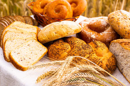 various types of fresh bread on linen tablecloth on table in cereal field outsideの写真素材