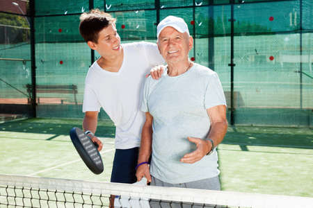Happy cheerful padel players of different generations talking on court playing paddleの写真素材