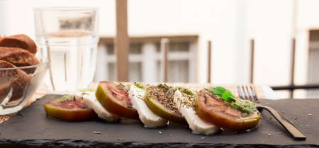 appetizing caprese salad with mozzarella, black tomatoes and pesto on black stone plate
